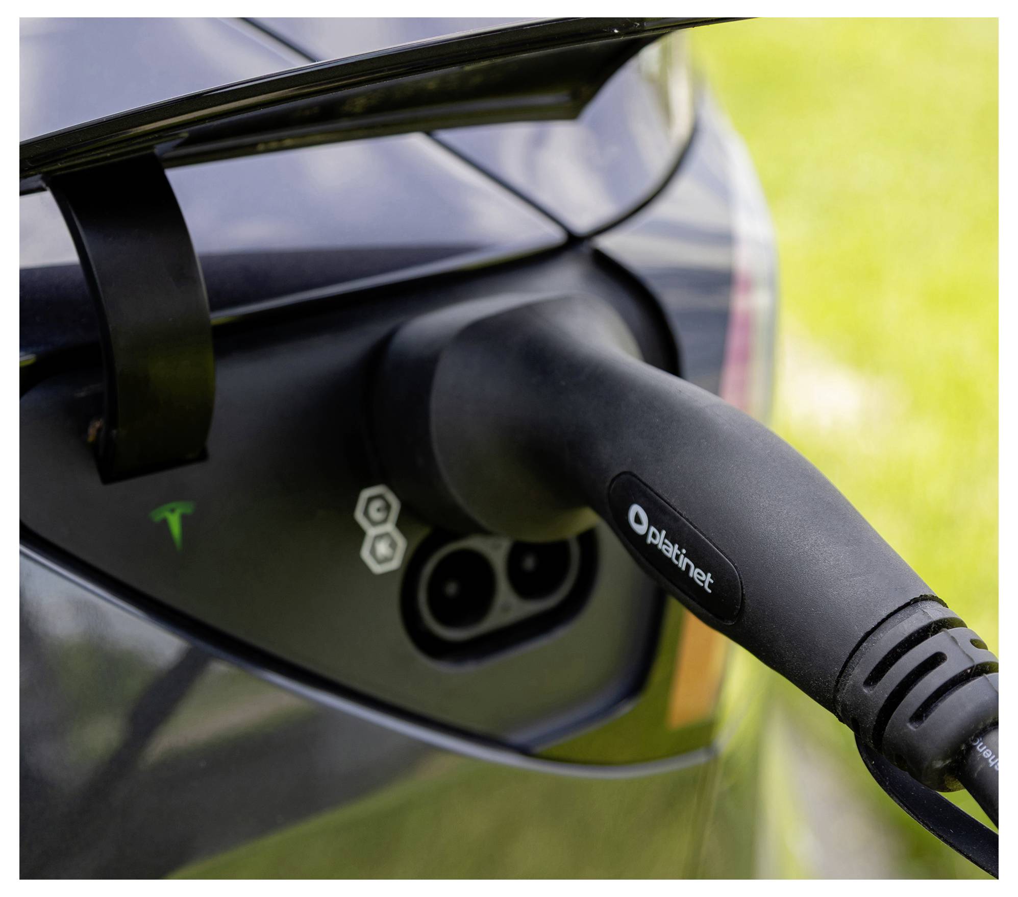 Une voiture électrique est en train de charger, avec un câble branché dans son port. Le logo sur la voiture indique qu'elle provient d'une marque notable de véhicules électriques.