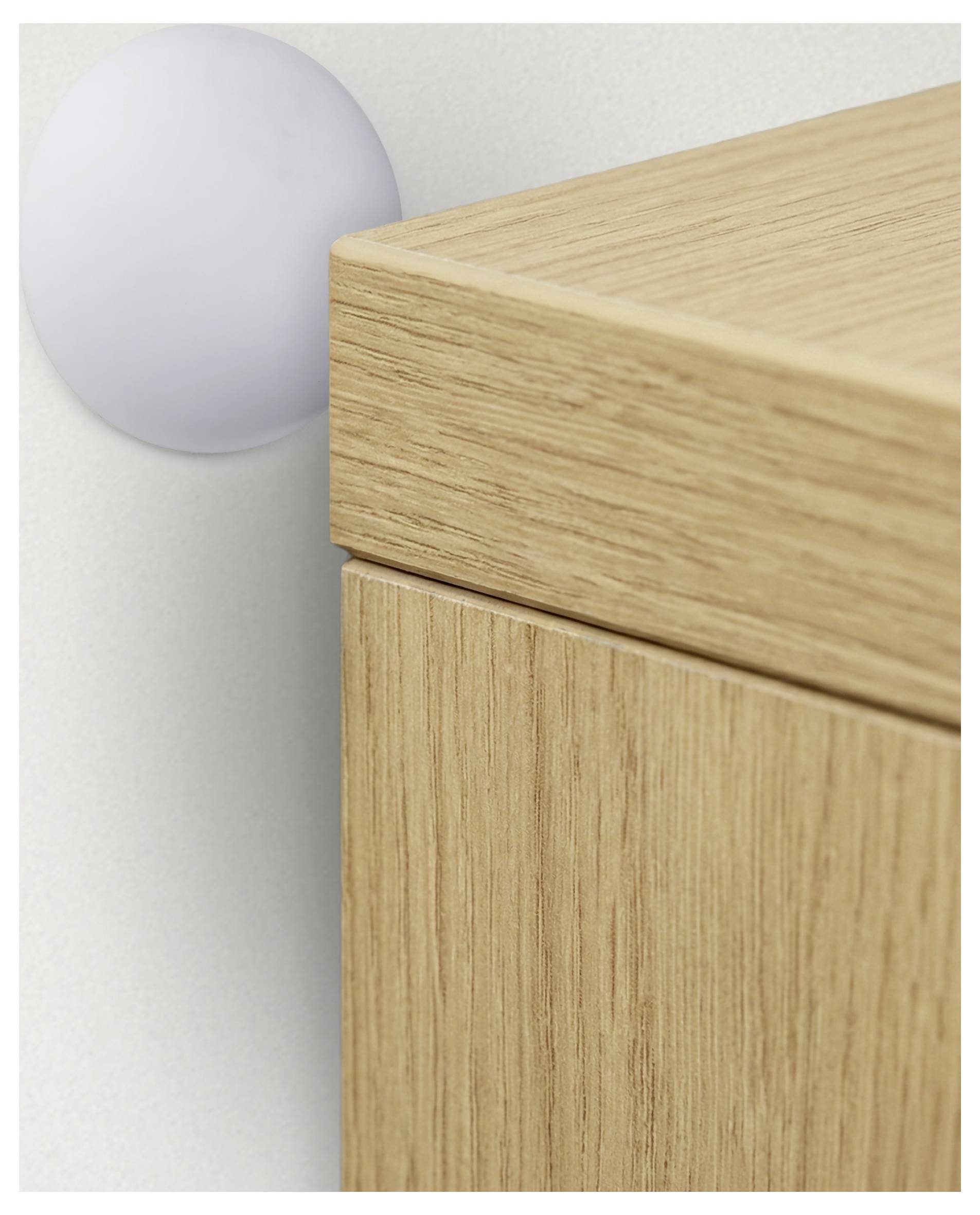 Un coin d'armoire en bois avec un protecteur mural circulaire blanc empêche les chocs contre le mur.