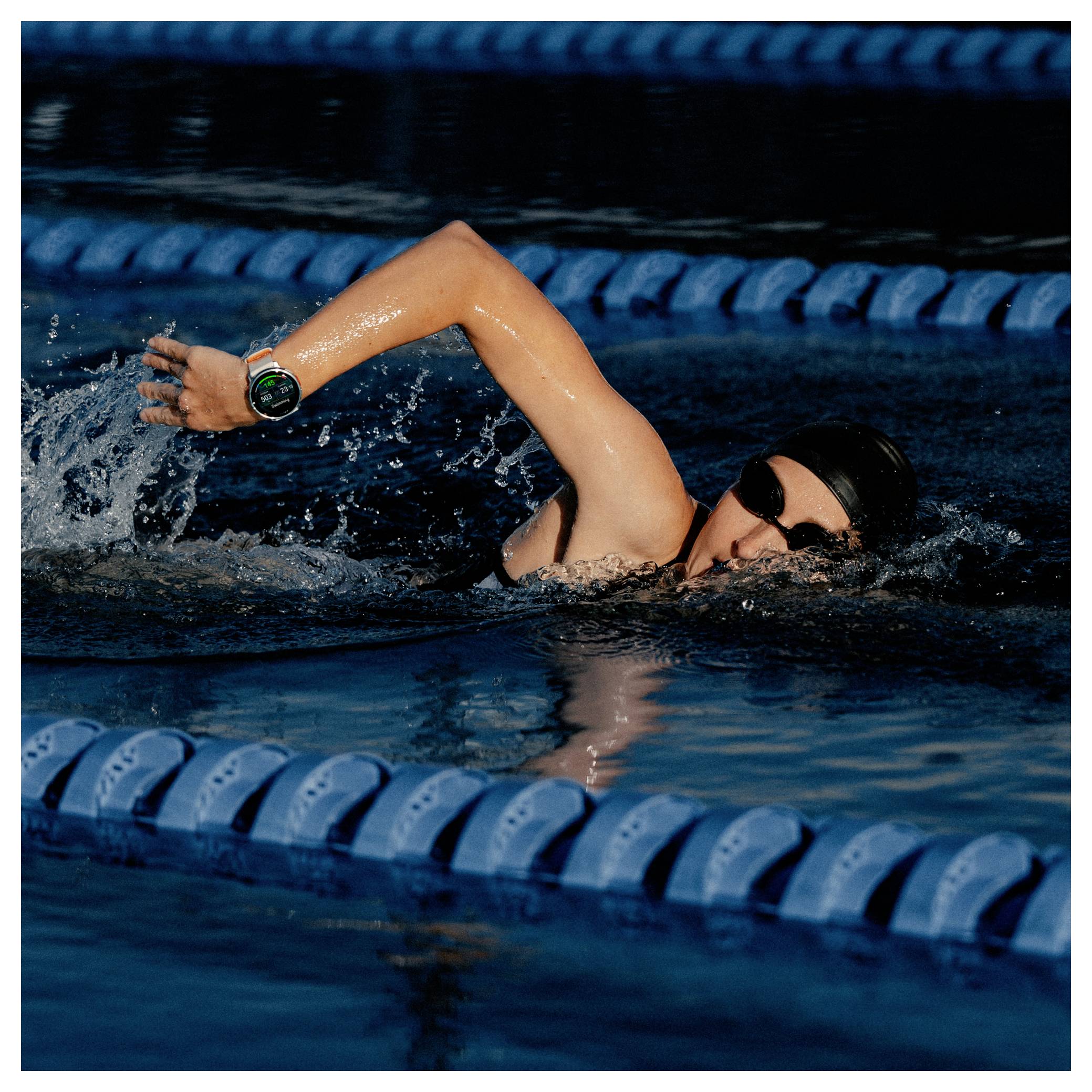 Un nageur dans une piscine effectuant un crawl, portant des lunettes de natation et un bonnet, avec des lignes de délimitation bleues visibles dans l'eau.