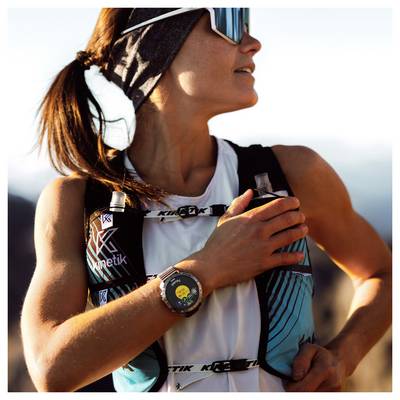 Une personne à l'extérieur portant un bandeau et des lunettes de soleil, regardant vers le haut tout en ajustant un tracker de fitness. La scène suggère de l'exercice ou une aventure.