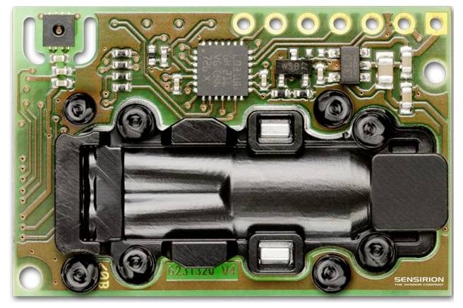 Circuit électronique avec un composant central noir, plusieurs petites puces électroniques et de multiples connecteurs. Le mot « SENSIRION » est visible.