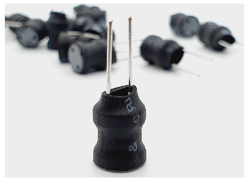 Un gros plan d'un composant électronique noir avec deux broches métalliques pointant vers le haut, d'autres composants similaires étant flous en arrière-plan.