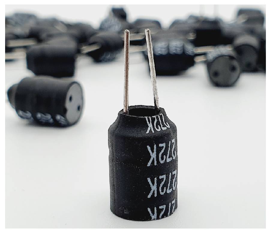 Un gros plan d'un composant électronique cylindrique noir avec deux connexions métalliques, entouré d'autres composants similaires en arrière-plan.