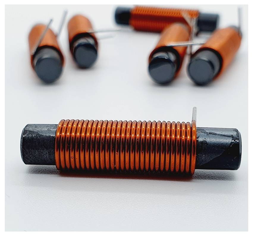 Gros plan d'un noyau cylindrique noir enroulé de fil de cuivre, avec plusieurs bobines similaires floues en arrière-plan.