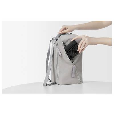 Une personne place une tablette dans un sac à dos gris posé sur une table blanche, démontrant la fonctionnalité de rangement du sac.