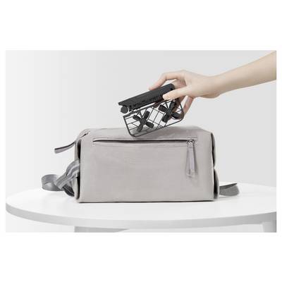 Une main place un drone compact et pliable dans un sac gris clair posé sur une table blanche, illustrant sa portabilité et sa facilité de rangement.