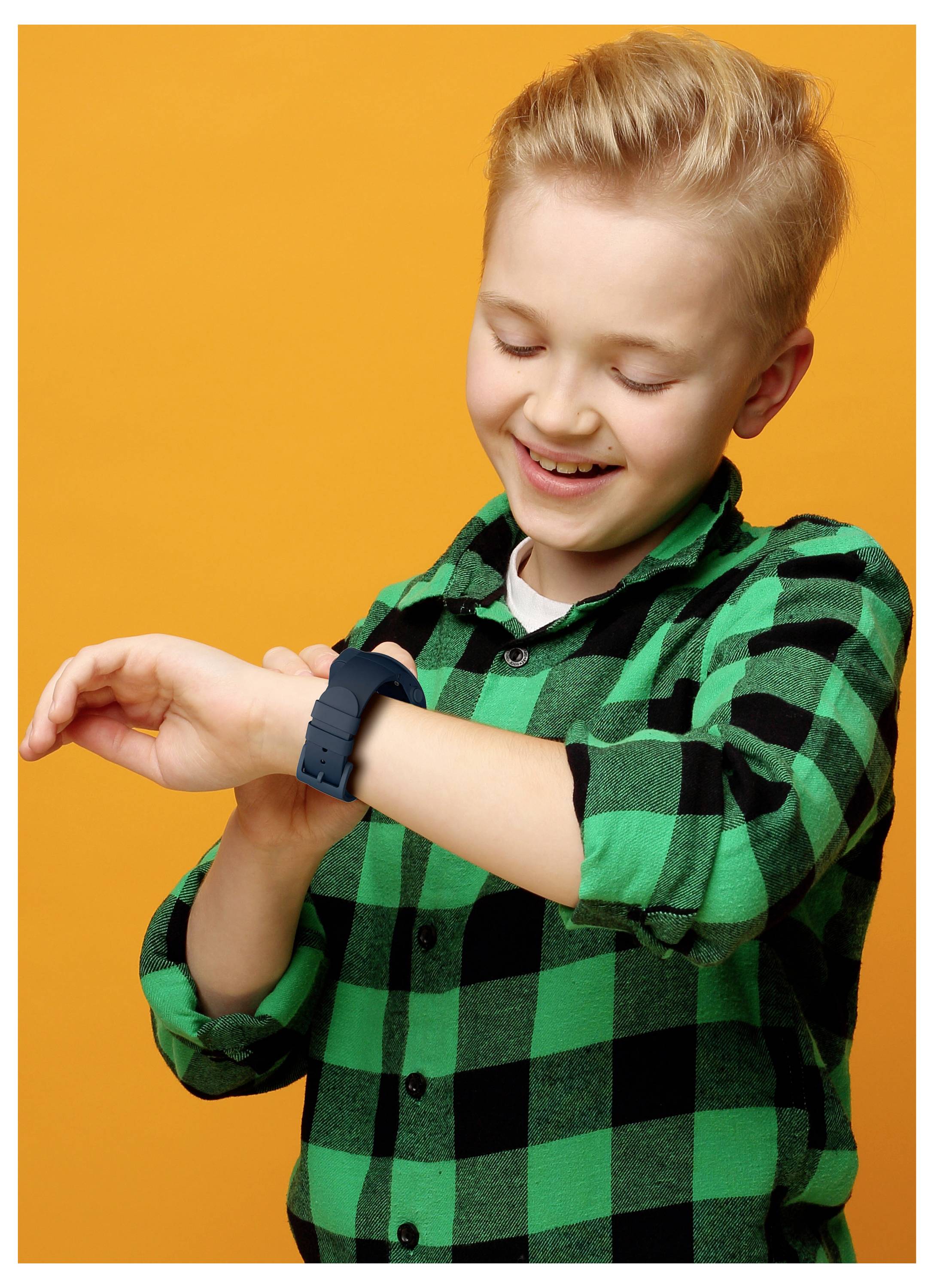 Un enfant souriant portant une chemise à carreaux verts regarde une montre intelligente à son poignet sur un fond orange.