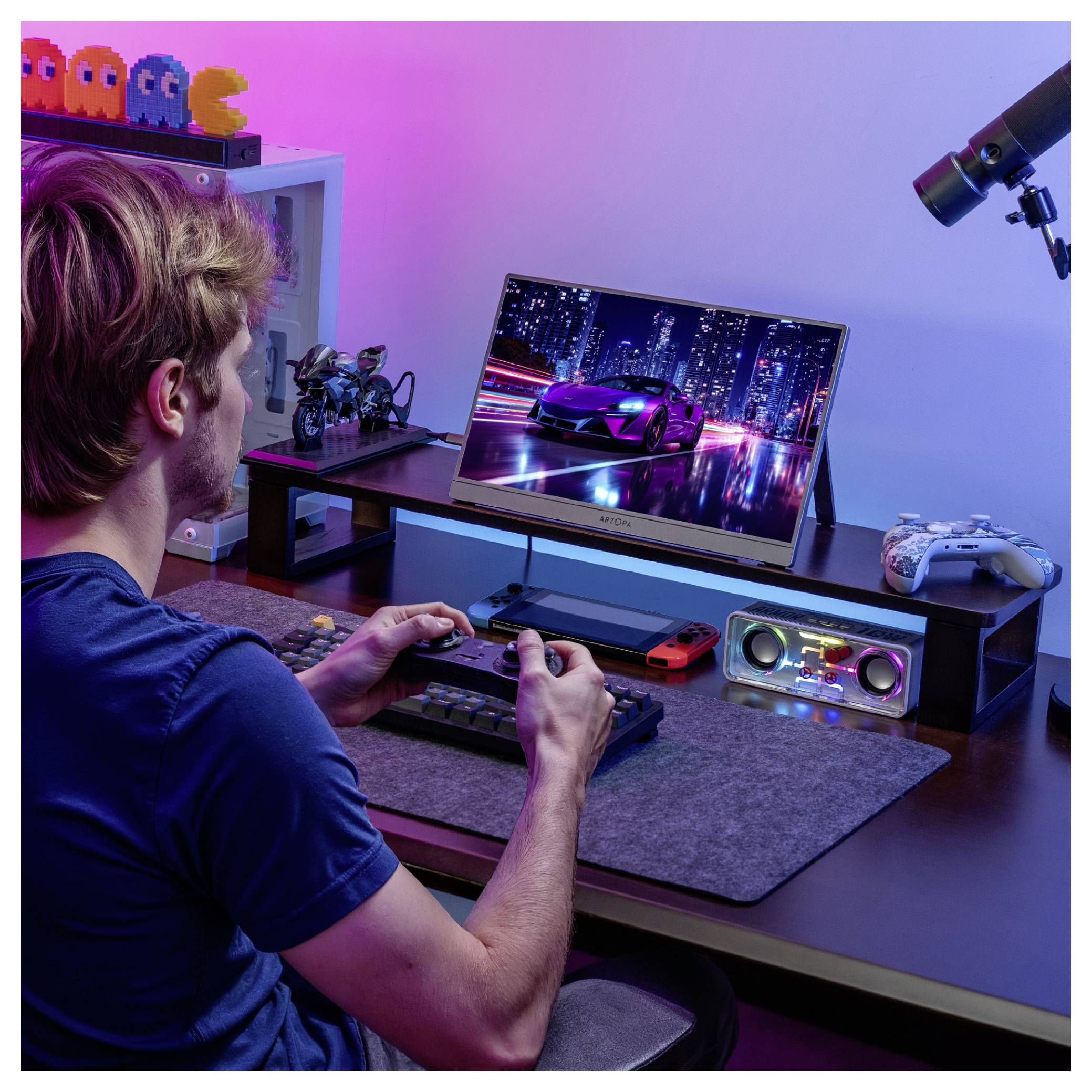 Une personne joue à un jeu de course sur un moniteur à un bureau avec des manettes de jeu, des enceintes et un télescope. Des personnages de jeux rétro sont rangés sur l'étagère.