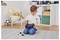 Un jeune garçon est à genoux sur un tapis, assemblant une voiture télécommandée avec un tournevis, entouré de jouets et d'un fauteuil rembourré dans une salle de jeux.