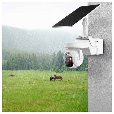 Une caméra de sécurité alimentée à l'énergie solaire, fixée sur un mur, surplombe un champ herbeux et pluvieux où des cerfs paissent en arrière-plan.