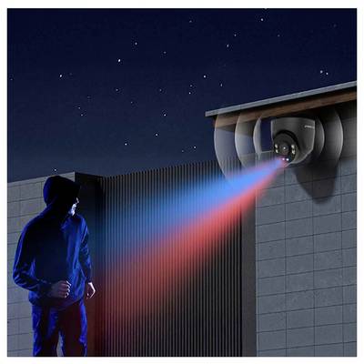 Une personne vêtue de vêtements sombres s'approche d'un bâtiment dans la nuit. Une caméra de sécurité émet une lumière bleue et rouge, signalant une détection.