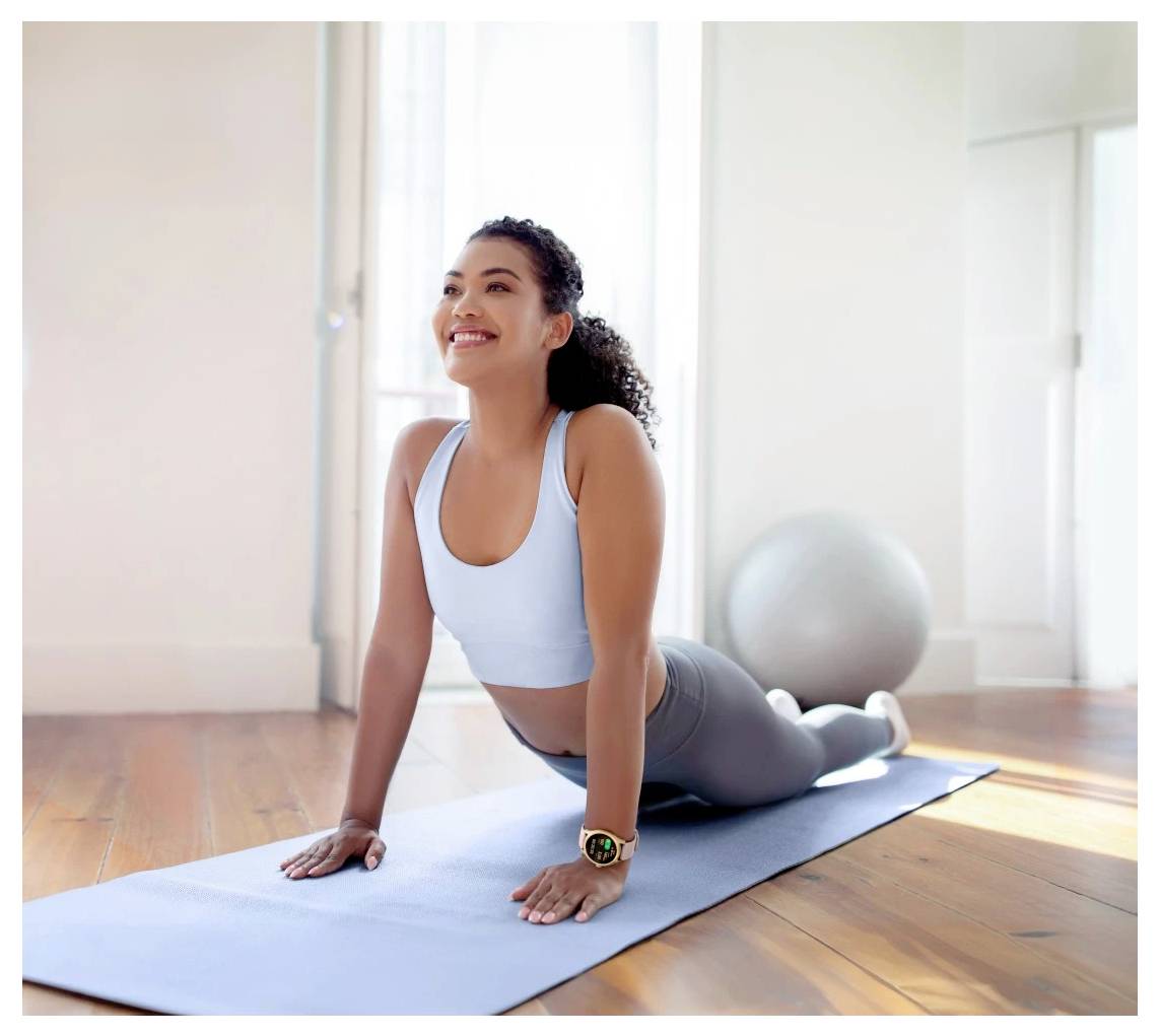 Une femme en tenue de sport pratique le yoga sur un tapis, effectuant une pose du cobra dans une pièce baignée de soleil, avec un ballon de gym en arrière-plan.