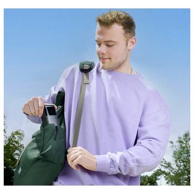 Une personne portant un sweat-shirt violet place une bouteille d'eau noire dans un sac à dos vert sur un fond de ciel bleu clair.