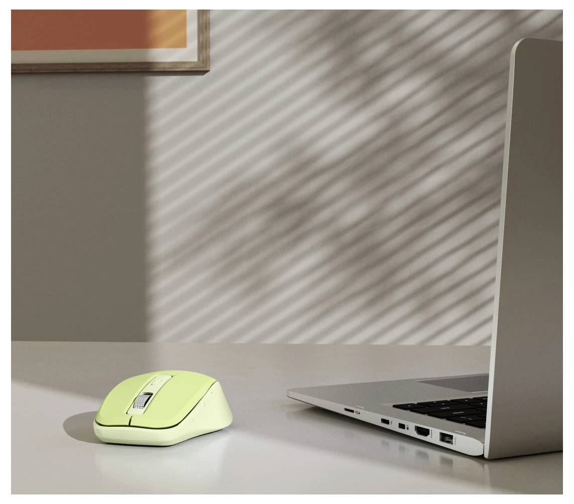 Une souris d'ordinateur jaune à côté d'un ordinateur portable argenté sur un bureau, avec de la lumière du soleil et des ombres créant des motifs sur le mur en arrière-plan.
