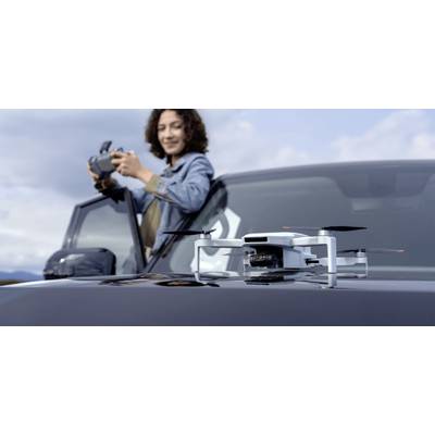Une personne contrôle un drone avec une télécommande, debout à côté d'un SUV. Le drone est posé sur le capot du véhicule, prêt à voler.