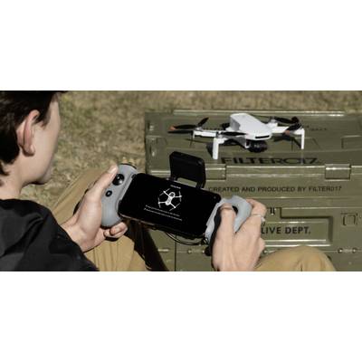 Une personne pilote un drone à l'aide d'une télécommande portable et d'un smartphone. Le drone est positionné sur un boîtier métallique vert portant l'étiquette « FILTER017 ».