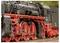 Gros plan sur le côté d'une locomotive à vapeur vintage, mettant en valeur ses grandes roues rouges et ses tuyauteries complexes en noir sur un fond estompé.