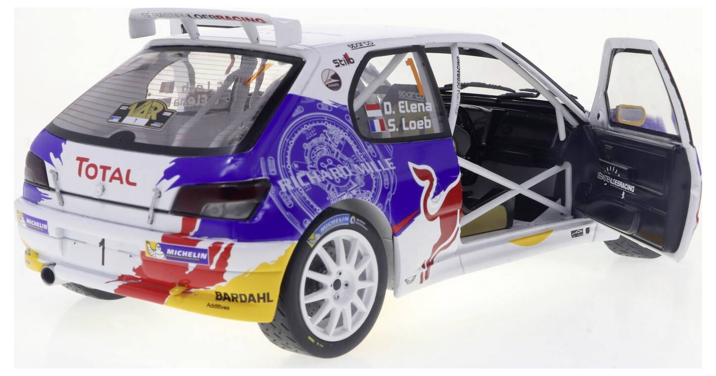 Une voiture de rallye miniature aux portes ouvertes met en valeur un design coloré, comprenant des logos de sponsors et des graphismes. À l'intérieur, une cage de sécurité est visible.