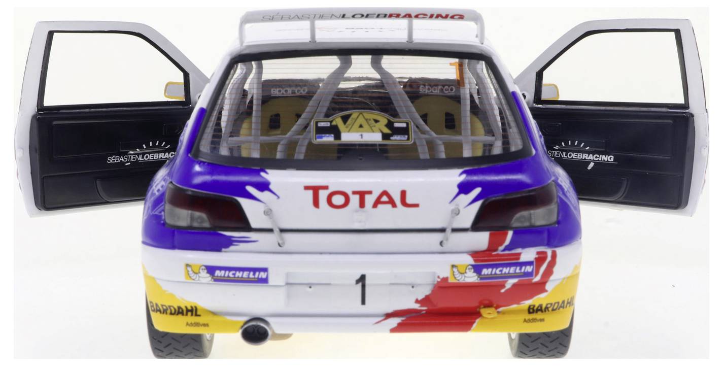 Voiture de rallye avec marquage 'Total', portes ouvertes, et un design vibrant rouge, bleu et jaune. La voiture arbore le numéro '1' sur sa partie arrière.