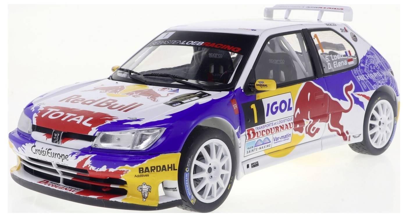 Une voiture de rallye avec les logos 'Red Bull' et 'Total', le numéro 1, et divers autocollants de sponsors. Elle est principalement blanche avec des touches de rouge et de bleu.