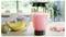 Un blender rempli d'un smoothie rose sur un comptoir de cuisine, entouré de bananes fraîches, de fraises, de kiwis et d'un bol de baies.
