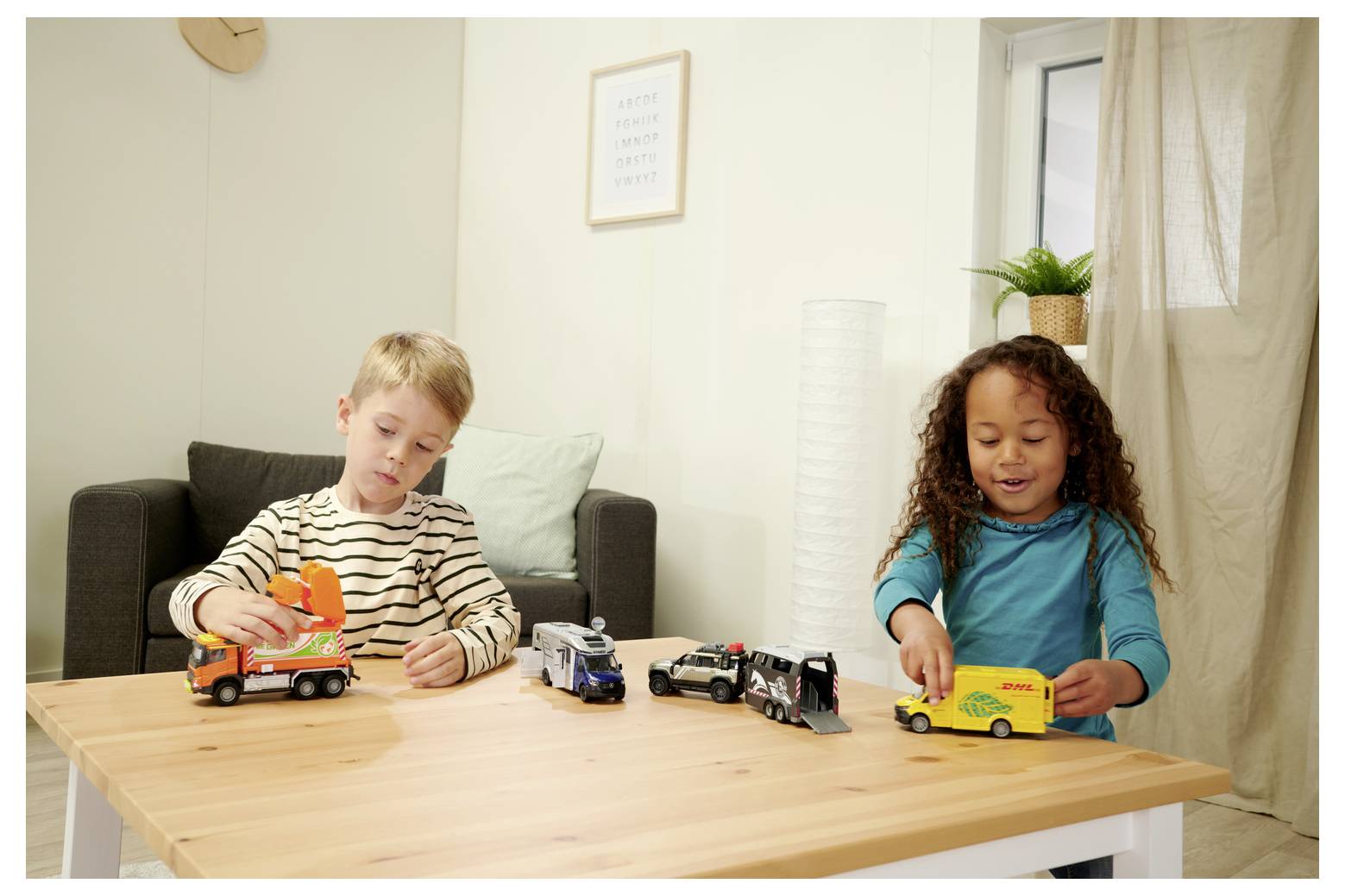 Deux enfants jouant à une table avec des véhicules miniatures dans un salon, avec un canapé, une plante et un tableau encadré en arrière-plan.