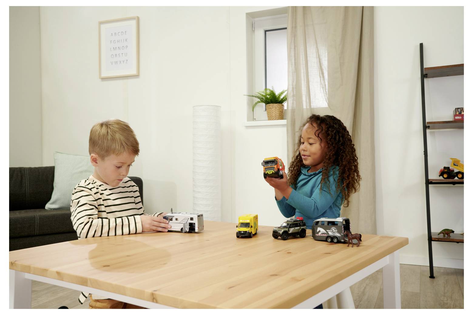 Une jeune fille et un garçon sont assis à une table, jouant avec des camions miniatures dans une pièce douillette. La fille tient un camion, tandis que le garçon examine un autre.