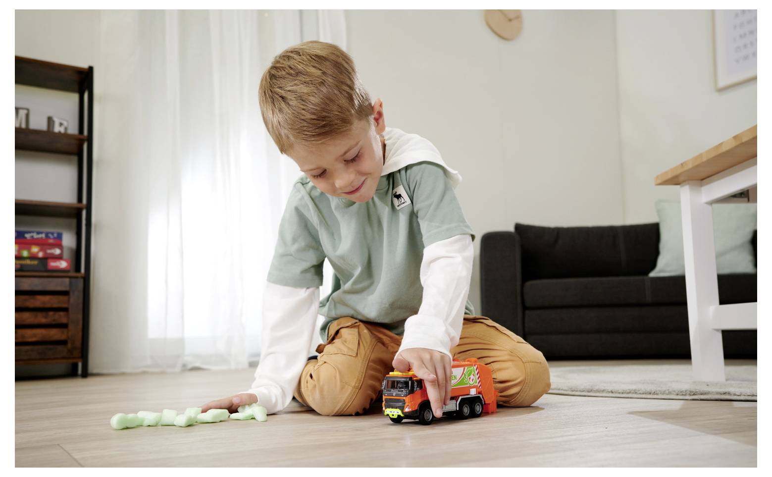 Un enfant joue avec un camion miniature sur un parquet dans un salon, entouré de quelques blocs de mousse éparpillés.