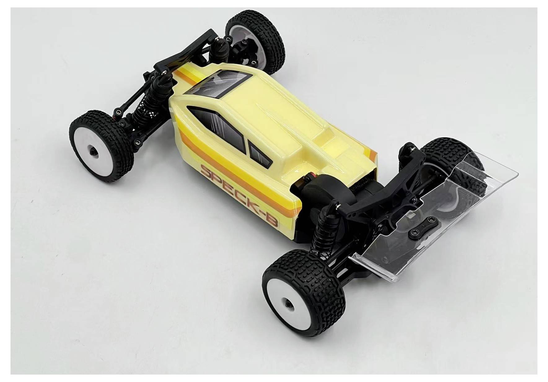 Une voiture télécommandée jaune et blanche, dotée de roues noires, est posée sur une surface blanche unie. La voiture présente un design élégant et aérodynamique.