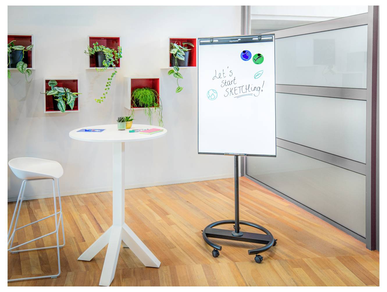 Une pièce lumineuse avec un tableau blanc mobile affichant le texte « Commençons à DESSINER ! » Une table ronde et des plantes décoratives sont à proximité.