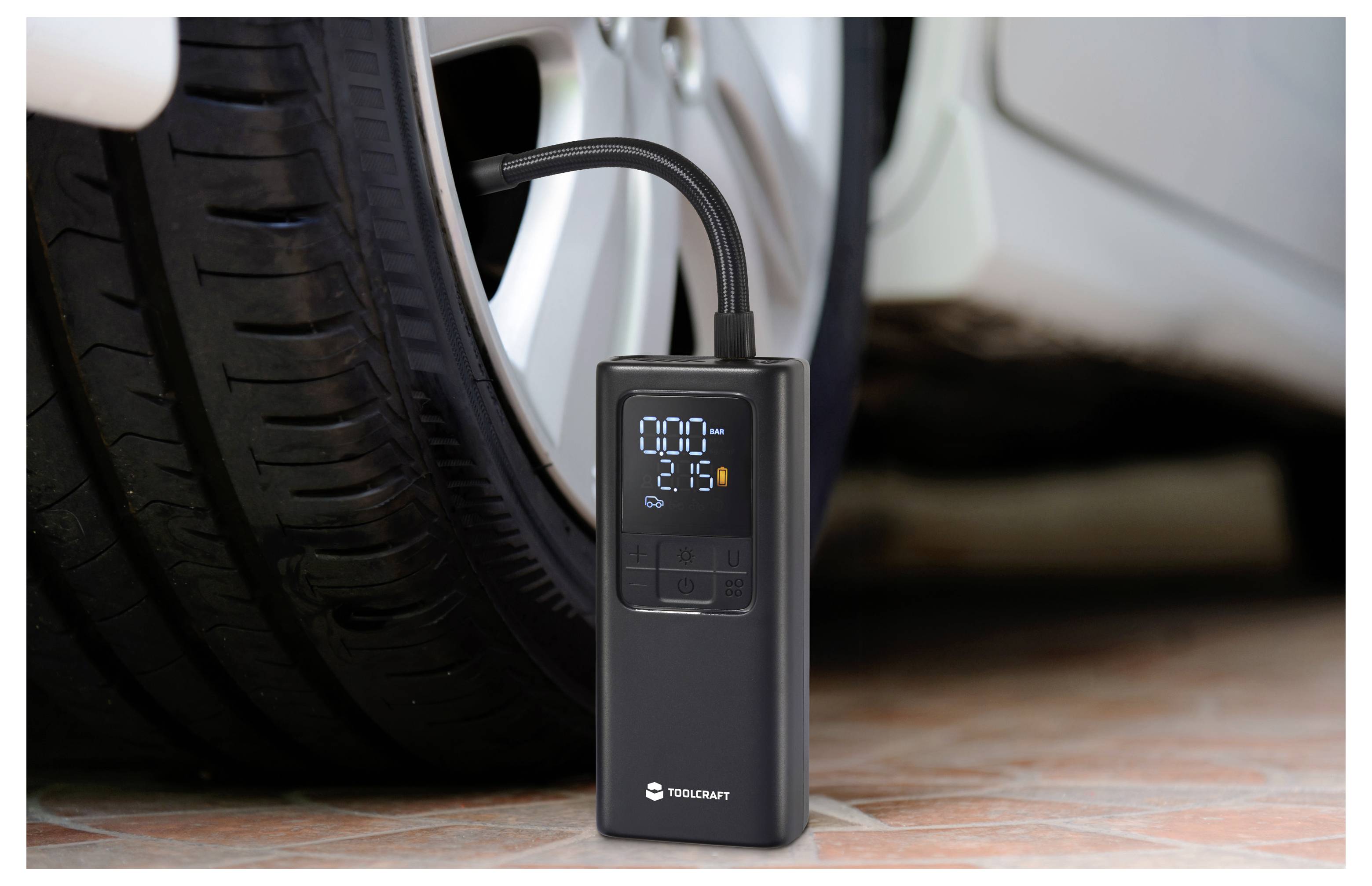 Gonfleur numérique portable connecté à un pneu de voiture, affichant un écran de pression allumé tandis que le véhicule est garé à l'intérieur.