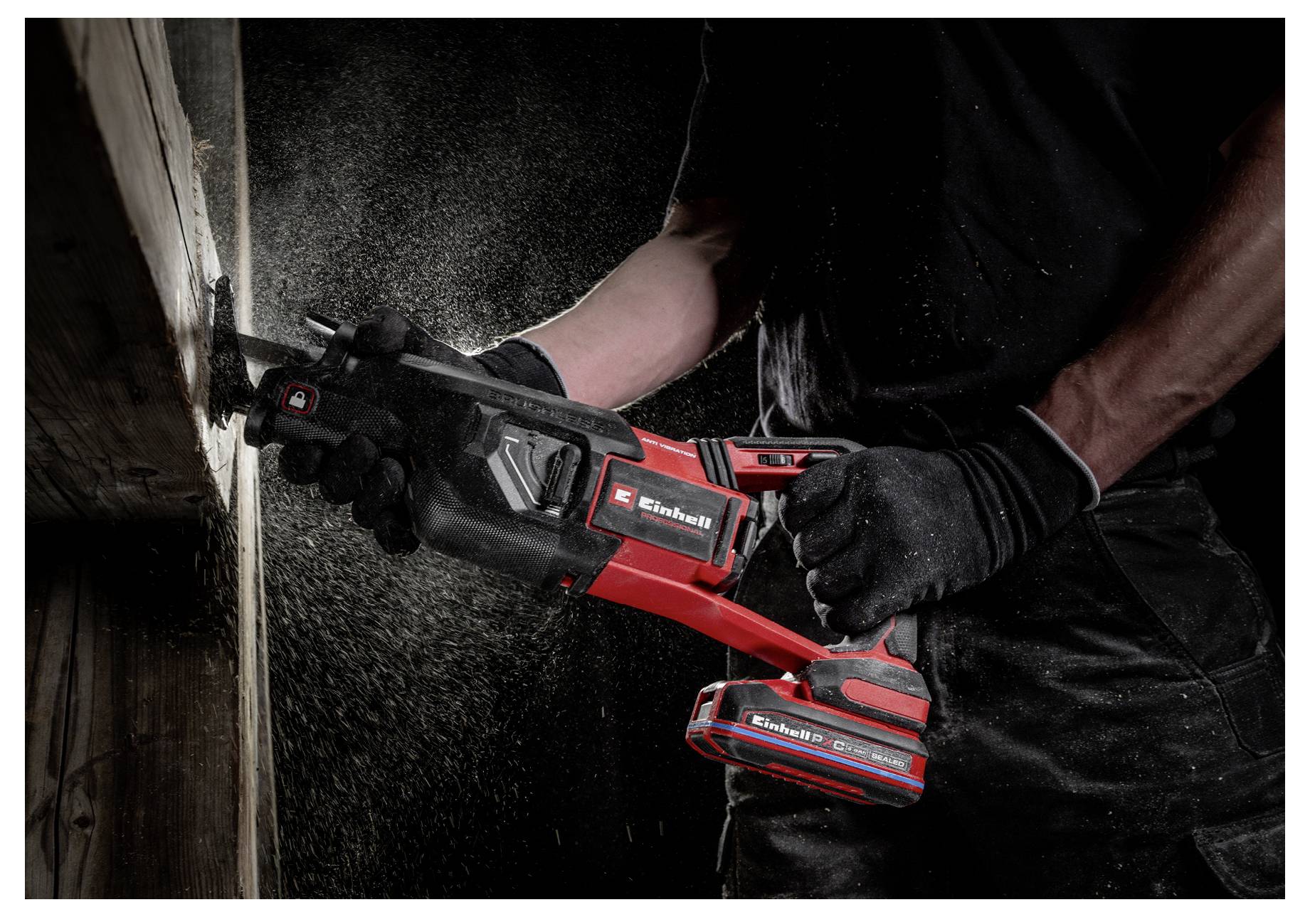 Une personne portant des gants utilise une scie sans fil rouge et noire pour couper une poutre en bois, avec de la sciure volant dans l'air.