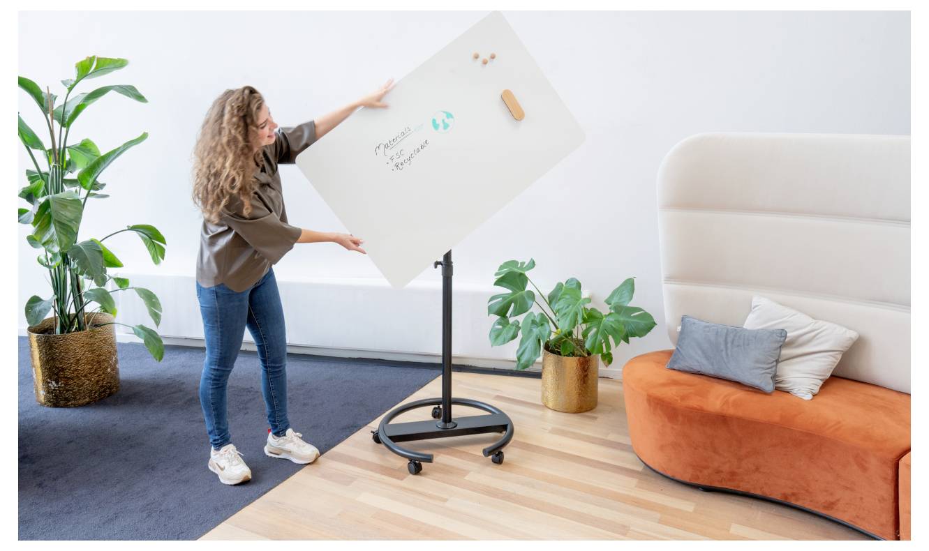 Une personne ajuste un tableau blanc rotatif sur lequel est inscrit « Planification de projet », près d'un canapé moderne et des plantes dans un bureau contemporain.