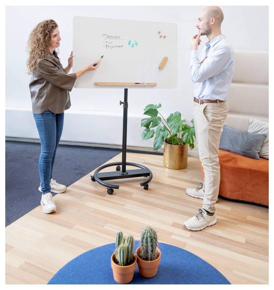 Une femme pointe du doigt un tableau blanc sur lequel est écrit « Objectifs du plan marketing », tandis qu'un homme l'écoute attentivement. Scène dans un bureau intérieur.