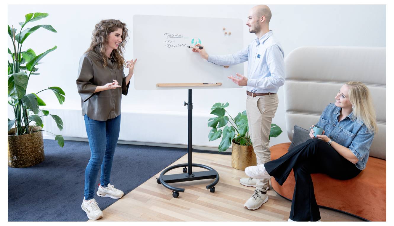 Trois personnes dans une salle de réunion décontractée ; l'un écrit sur un tableau blanc tandis qu'un autre se tient debout et fait des gestes, et la troisième personne est assise et observe.