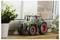 Un tracteur miniature avec de grandes roues rouges est posé sur une étagère en bois près d'une fenêtre, entouré de plantes vertes.