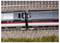 Vue aérienne de deux wagons de train connectés sur des voies parallèles, avec des environs industriels et champêtres.