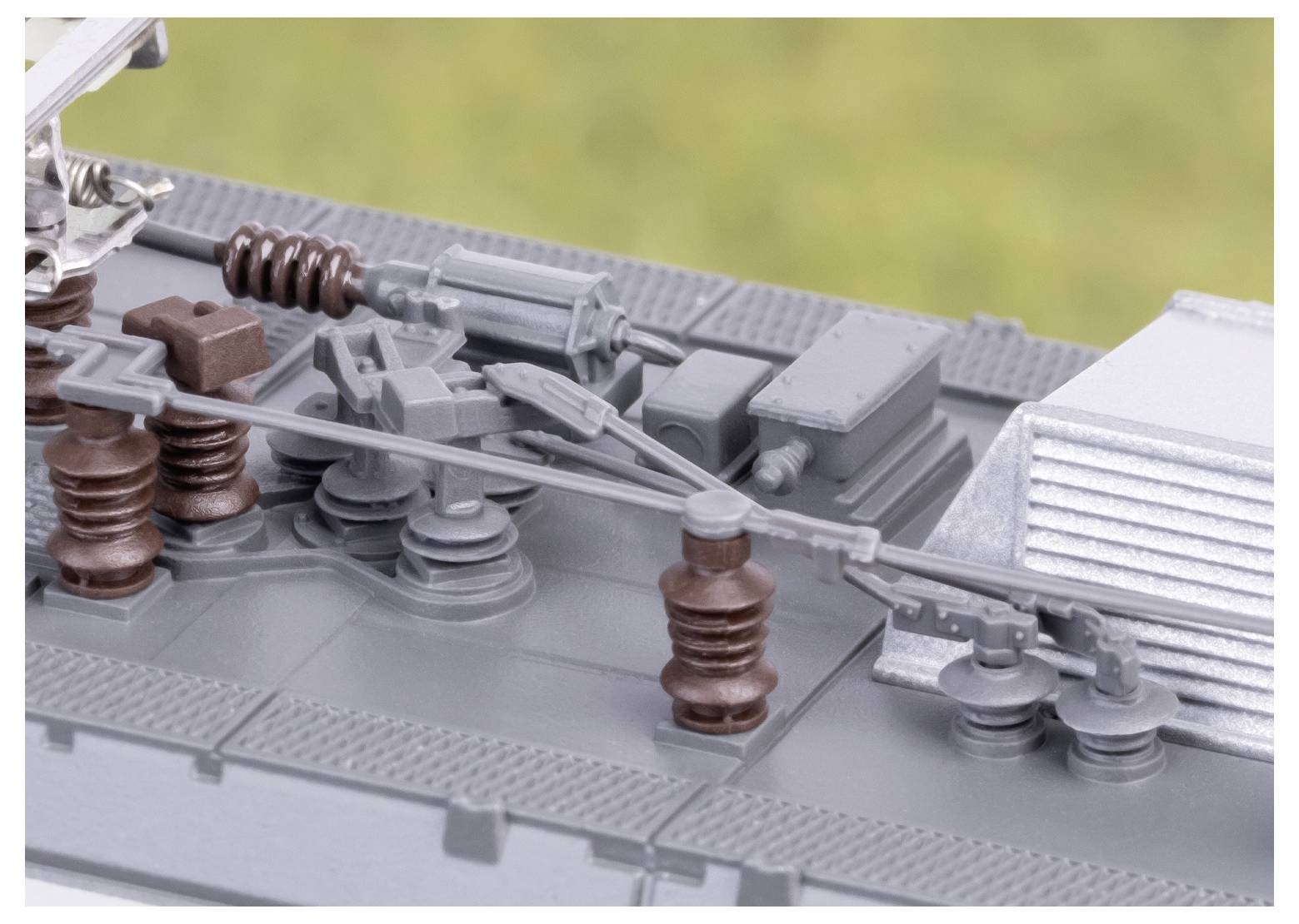 Gros plan sur le toit d'un train miniature montrant des détails intriqués avec des câbles, des isolateurs et des composants mécaniques sur un fond flou.