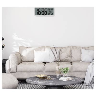 Un salon contemporain présente un canapé beige, une table basse ronde noire avec des plantes, et une horloge murale numérique affichant « 16:36, 25-12 ».