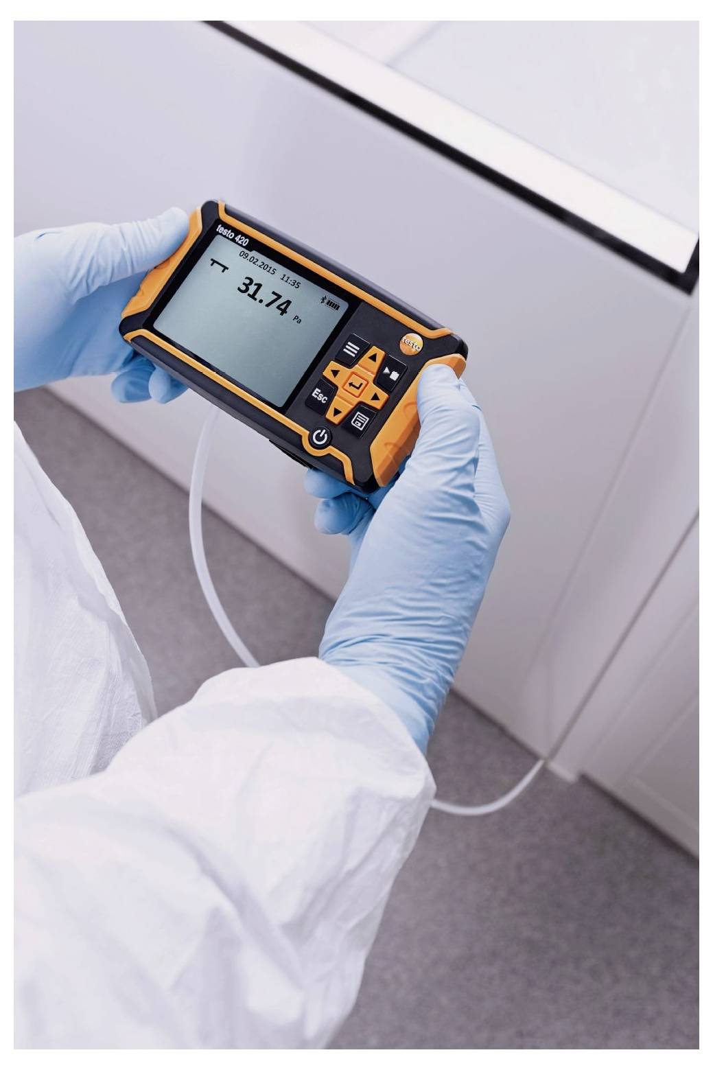 Une personne portant un équipement de protection tient un appareil numérique affichant '31,2 °C', mesurant probablement la température, et relié à des tubes dans un environnement de laboratoire.