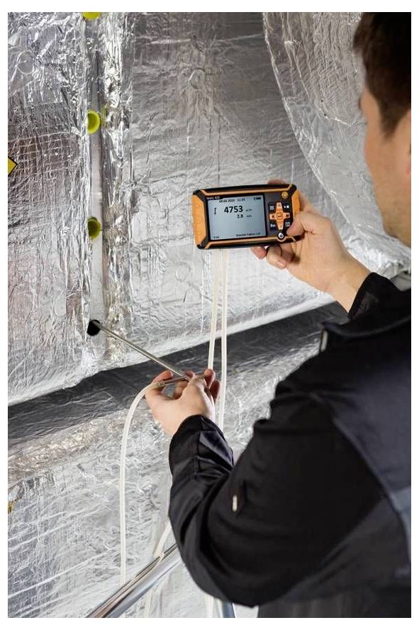 Une personne utilisant un appareil portable pour mesurer la qualité de l'air dans un conduit avec isolation réfléchissante. L'appareil affiche une lecture de « 4753 ».