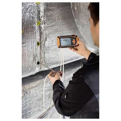 Une personne utilisant un appareil portable pour mesurer la qualité de l'air dans un conduit avec isolation réfléchissante. L'appareil affiche une lecture de « 4753 ».