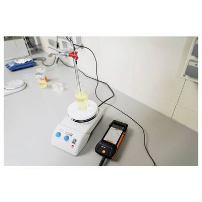 Un montage de laboratoire montre un bécher sur un agitateur magnétique avec un thermomètre numérique mesurant la température du liquide. Du matériel l'entoure.