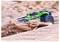 Un camion monstre télécommandé avec un design vert et noir roule à travers le sable, soulevant un panache de poussière dans un environnement extérieur.
