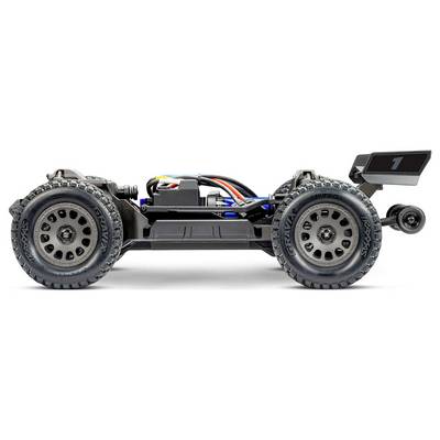 Vue de côté d'une petite voiture télécommandée noire, montrant des roues et des câblages détaillés. La voiture est élégante avec un aileron à l'arrière.