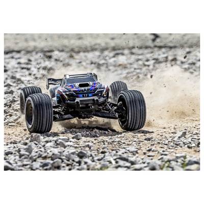 Une voiture télécommandée se déplace rapidement sur un terrain rocailleux, soulevant de la poussière. La voiture dispose de grandes roues et d'un design élégant.