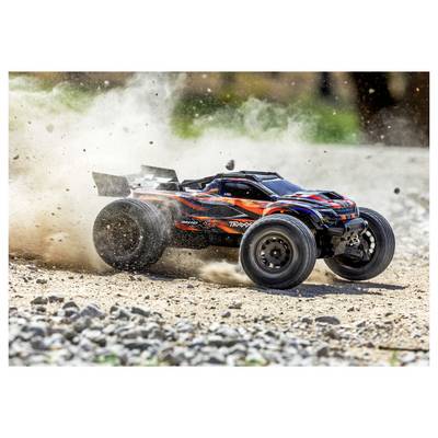 Une voiture télécommandée roule à toute vitesse sur un terrain rocailleux, soulevant des nuages de poussière. La voiture arbore un design noir et orange avec de grandes roues.