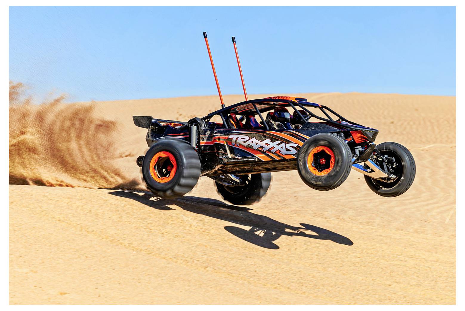 Une voiture télécommandée au design orange et noir franchit des dunes de sable, laissant derrière elle un nuage de poussière sur un ciel bleu dégagé.