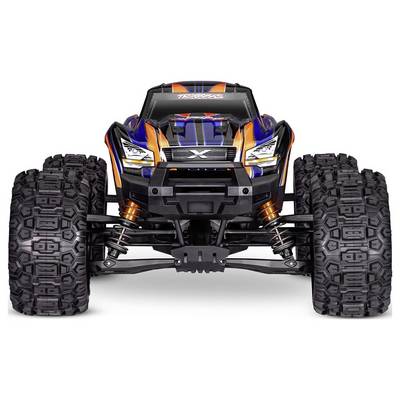 Un camion monstre télécommandé avec des pneus texturés de grande taille, et une carrosserie vibrante orange et bleue, vu de face.