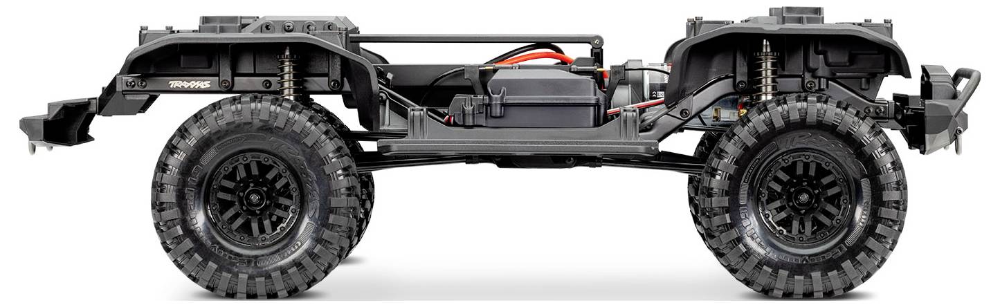 Vue latérale d'un châssis de voiture télécommandée avec de grandes roues tout-terrain, suspension visible, pack de batterie et composants moteur.